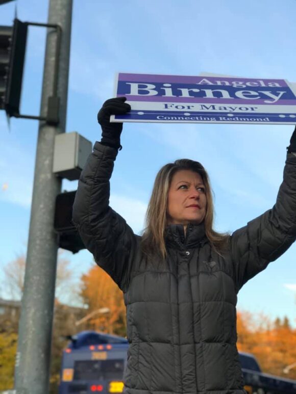 Angela holding her campaign sign at a street corner